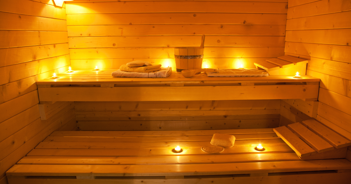 A cozy wooden sauna with lit candles, towels, and a water bucket, ready for a relaxing session.