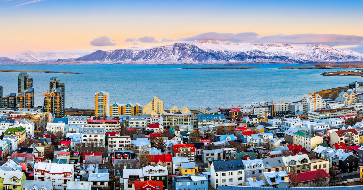 A panoramic view of Reykjavik, Iceland, with colorful houses, a bay, and snow-capped mountains in the distance.