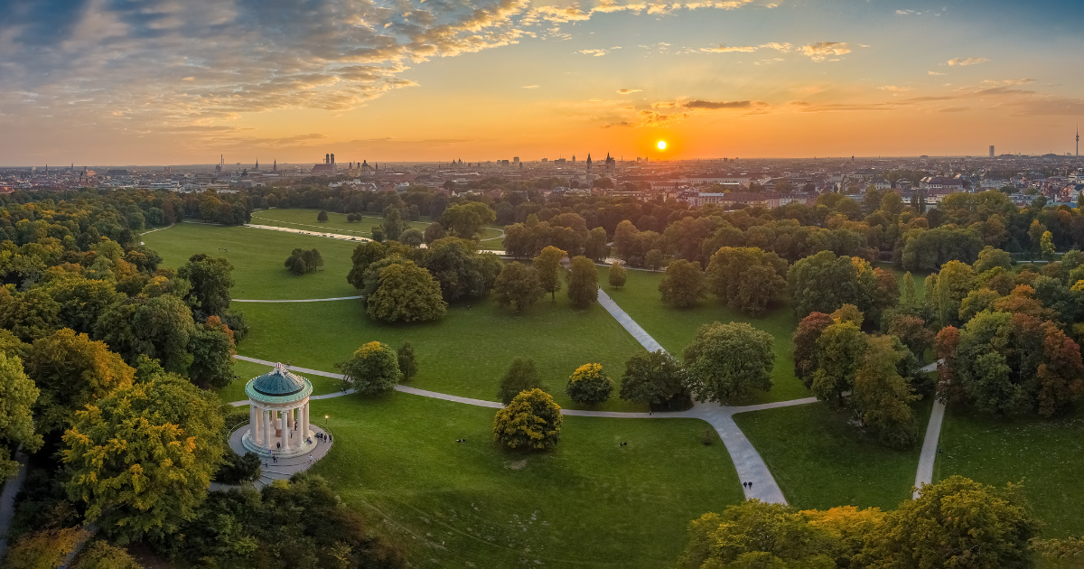 A breathtaking sunset view of the English Garden in Munich, with the city skyline in the distance and the Monopteros temple in the foreground.