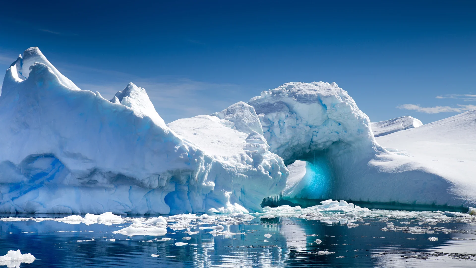 A large iceberg with a natural arch, floating in the ocean in Antarctica.