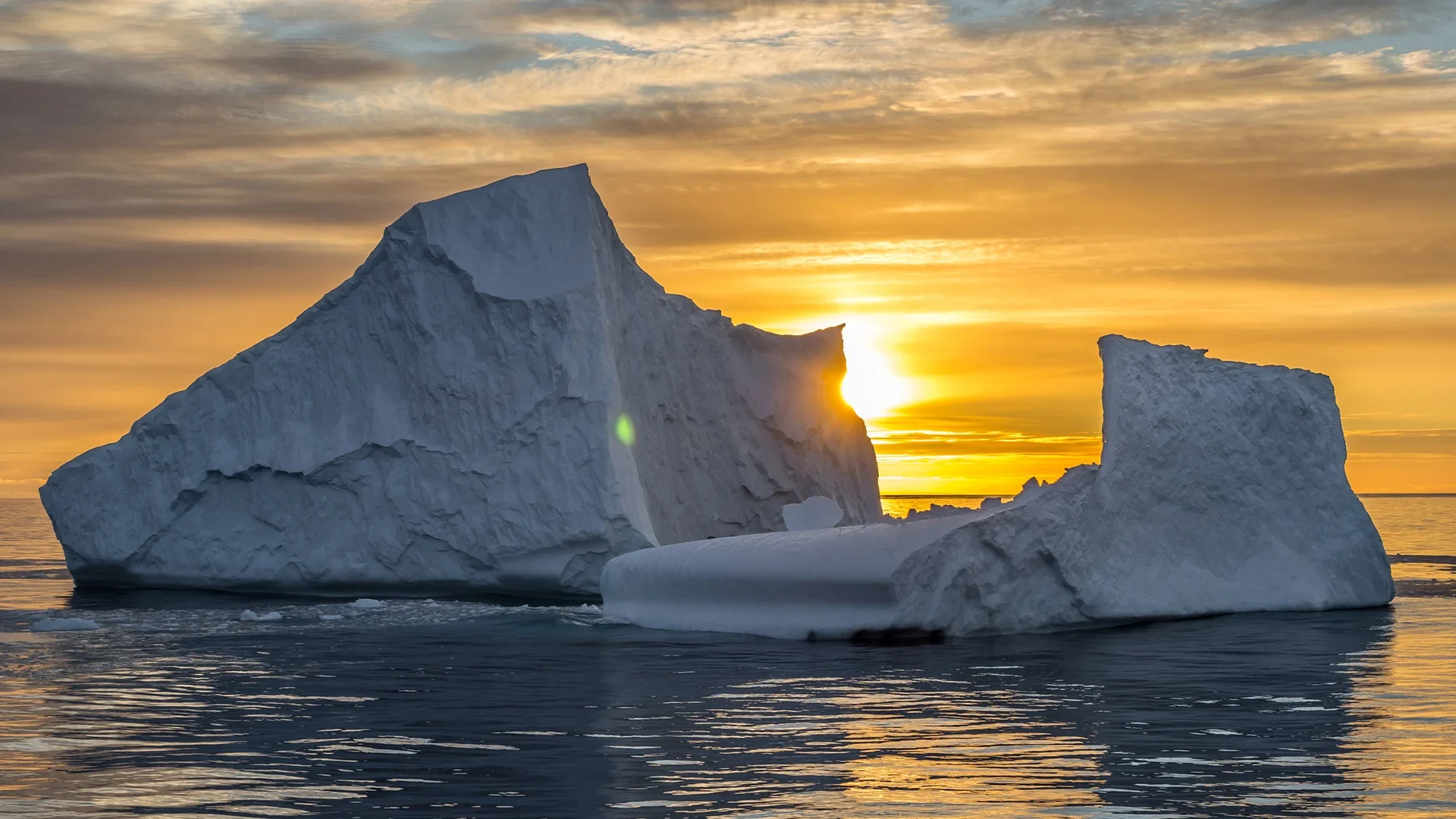 A dramatic sunset over a group of large icebergs in the Arctic Ocean.