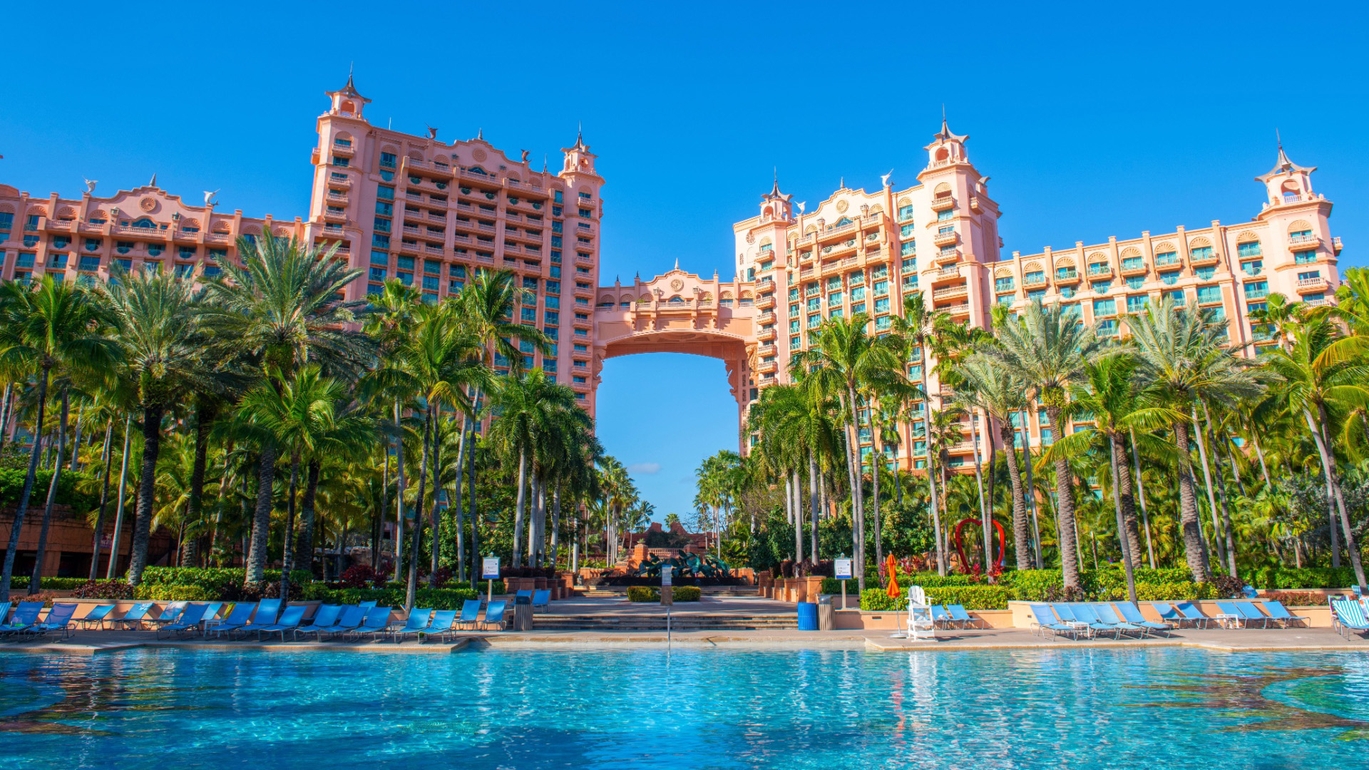 The iconic Atlantis Paradise Island resort in the Bahamas, showcasing its pink buildings, palm trees, and a large swimming pool.