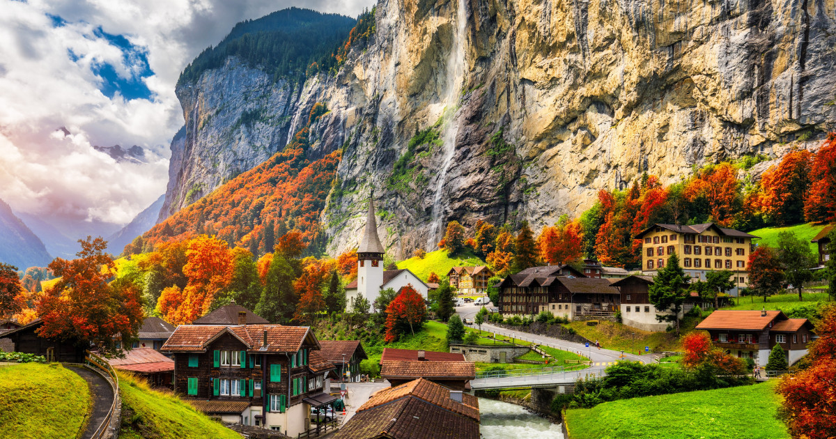 Lauterbrunnen Valley in Switzerland, with a cascading waterfall, colorful autumn foliage, and charming houses.