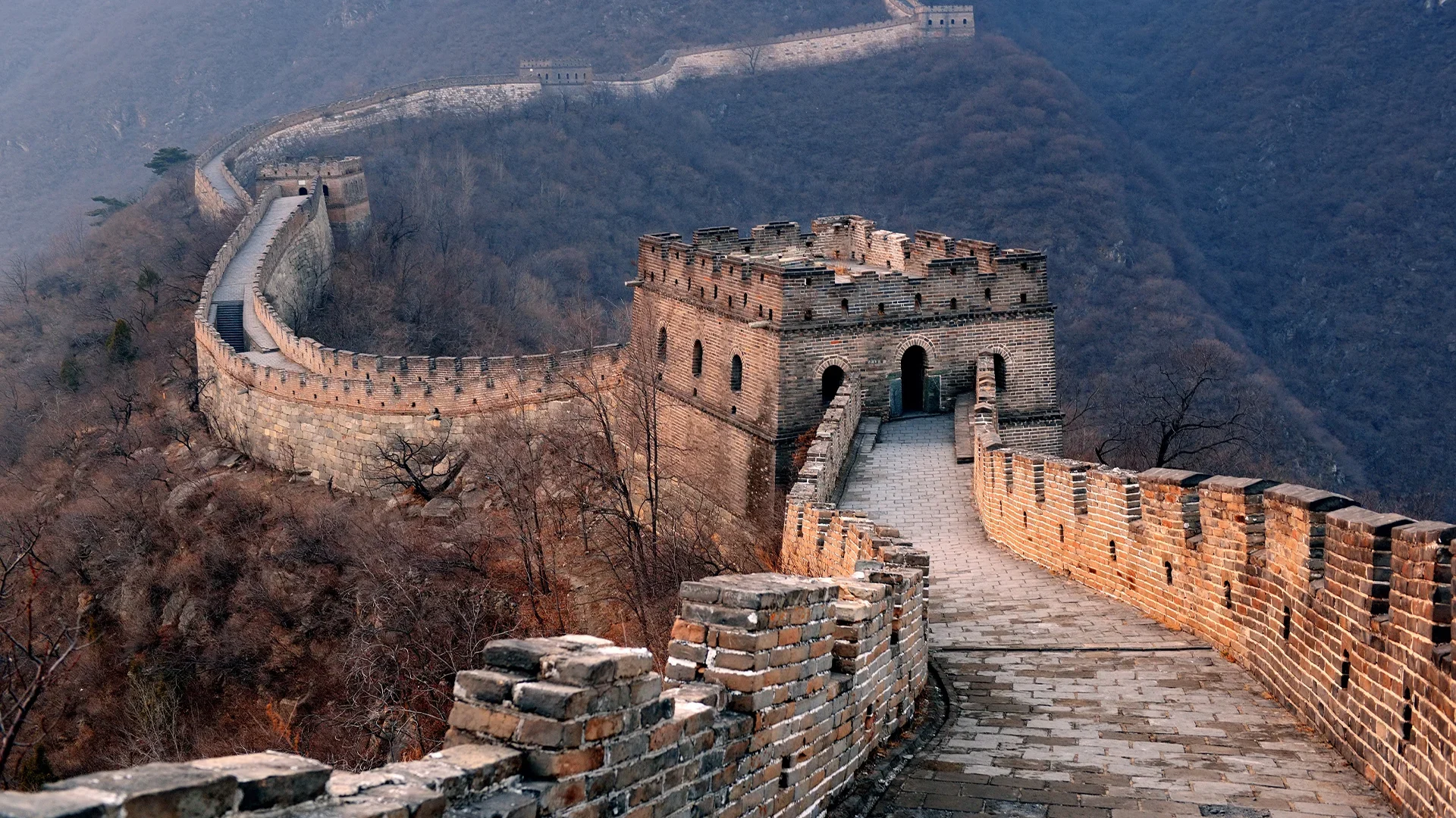 A winding section of the Great Wall of China with a watchtower, leading through a mountain pass.