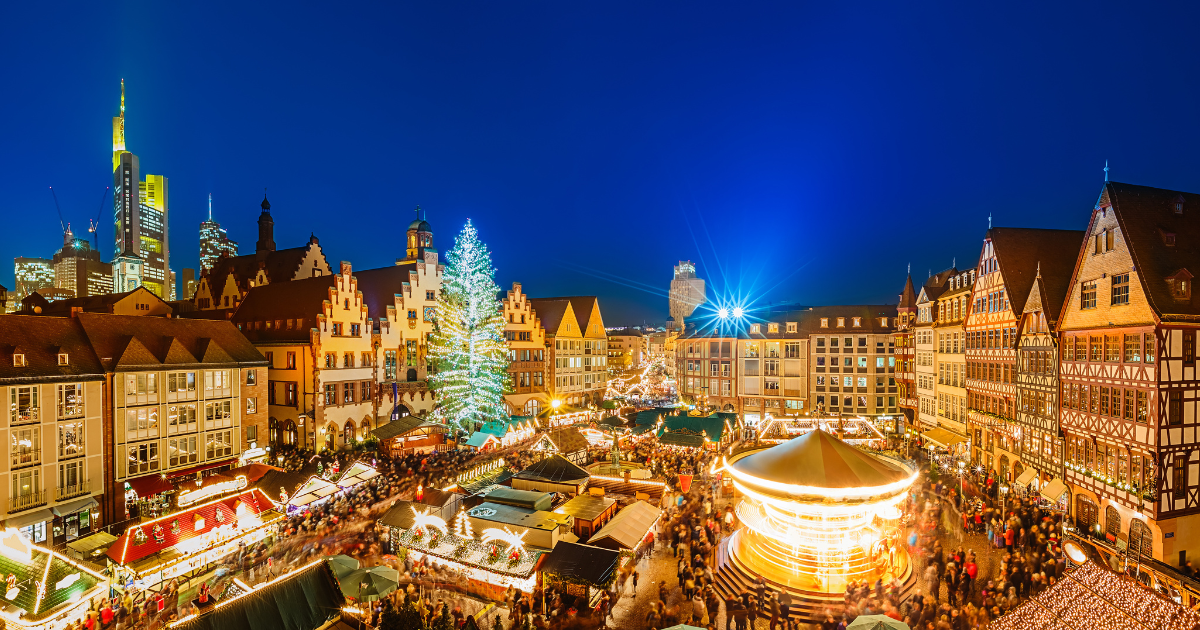 The Frankfurt Christmas Market at night, with the illuminated Römerberg square, the Christmas tree, and the Frankfurt skyline in the background.