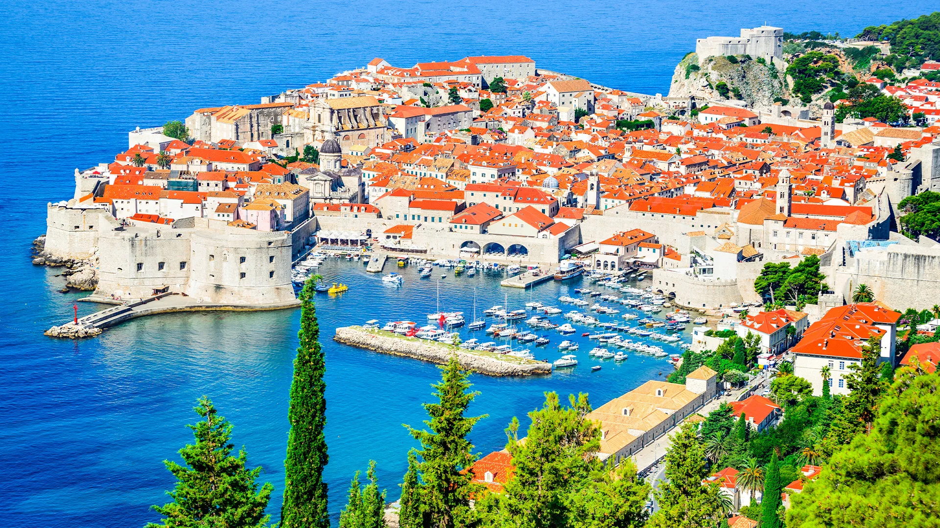 An aerial view of Dubrovnik, Croatia, showcasing its iconic city walls, red-tiled roofs, and the crystal-clear Adriatic Sea.