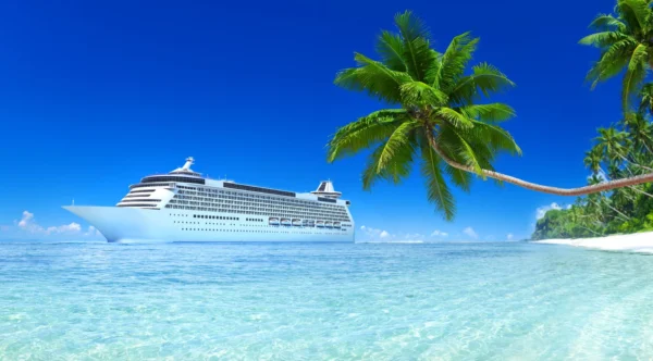 A large cruise ship sailing in the ocean near a tropical beach with palm trees.