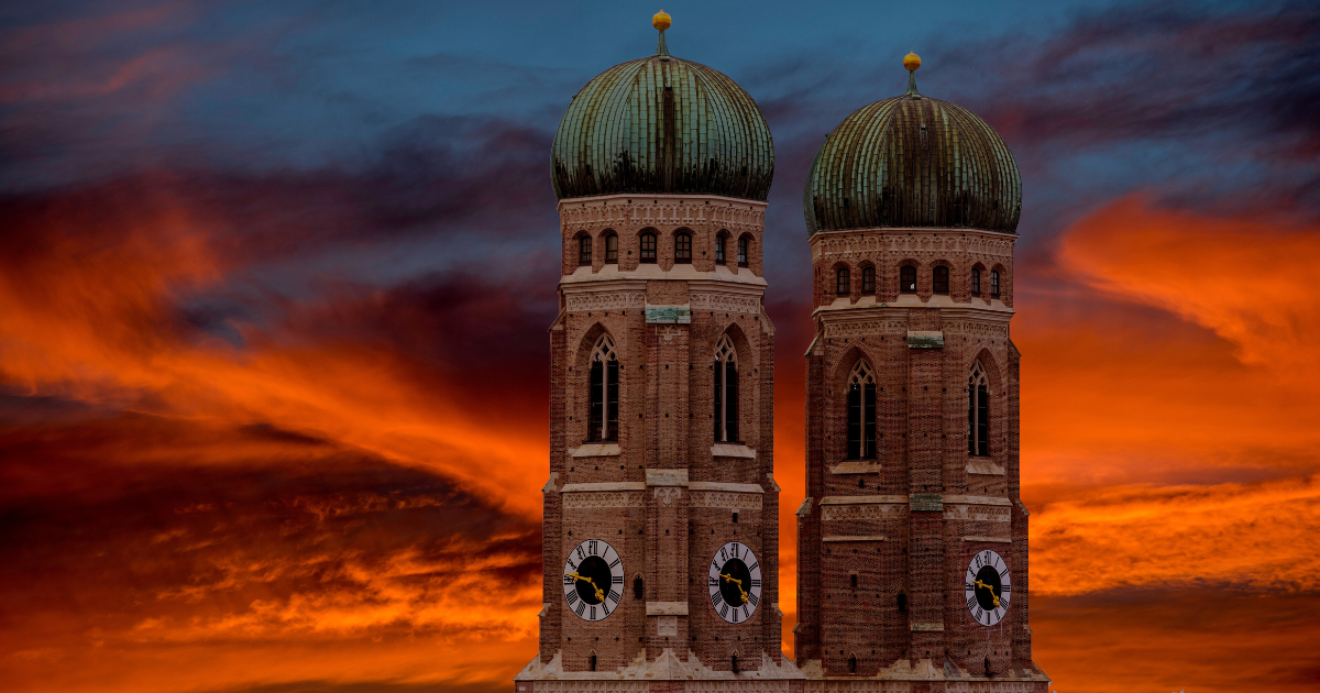 The iconic twin towers of the Frauenkirche in Munich, illuminated by a dramatic sunset sky.