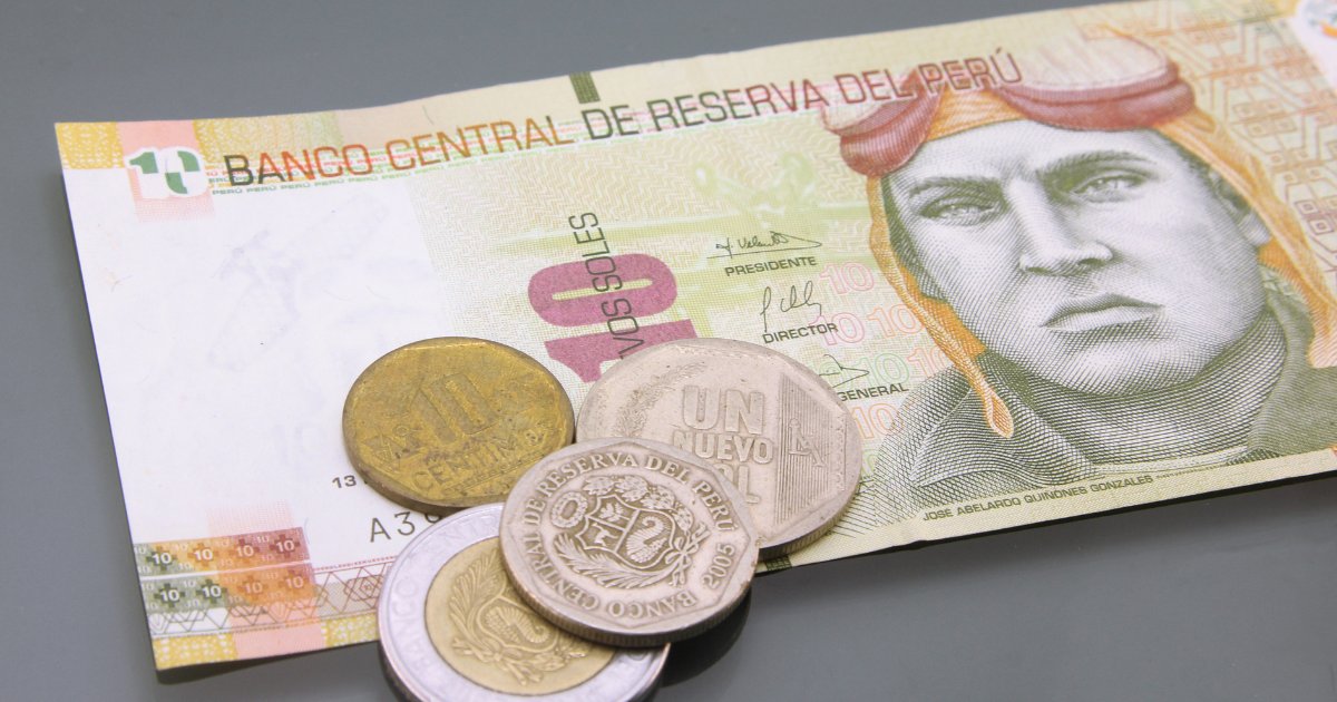 A Peruvian ten-sol note featuring the portrait of Jorge Chávez, along with several Peruvian coins.