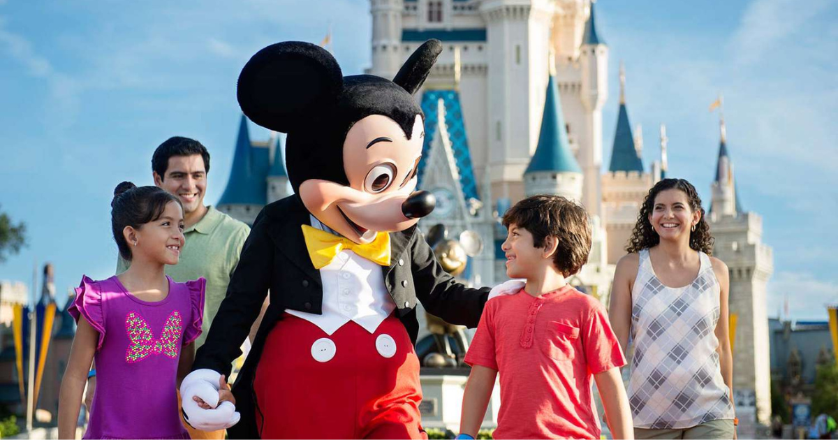 Family on a Disney Holiday, walking in front of Disney castle, smiling and holding hands with Mickey Mouse