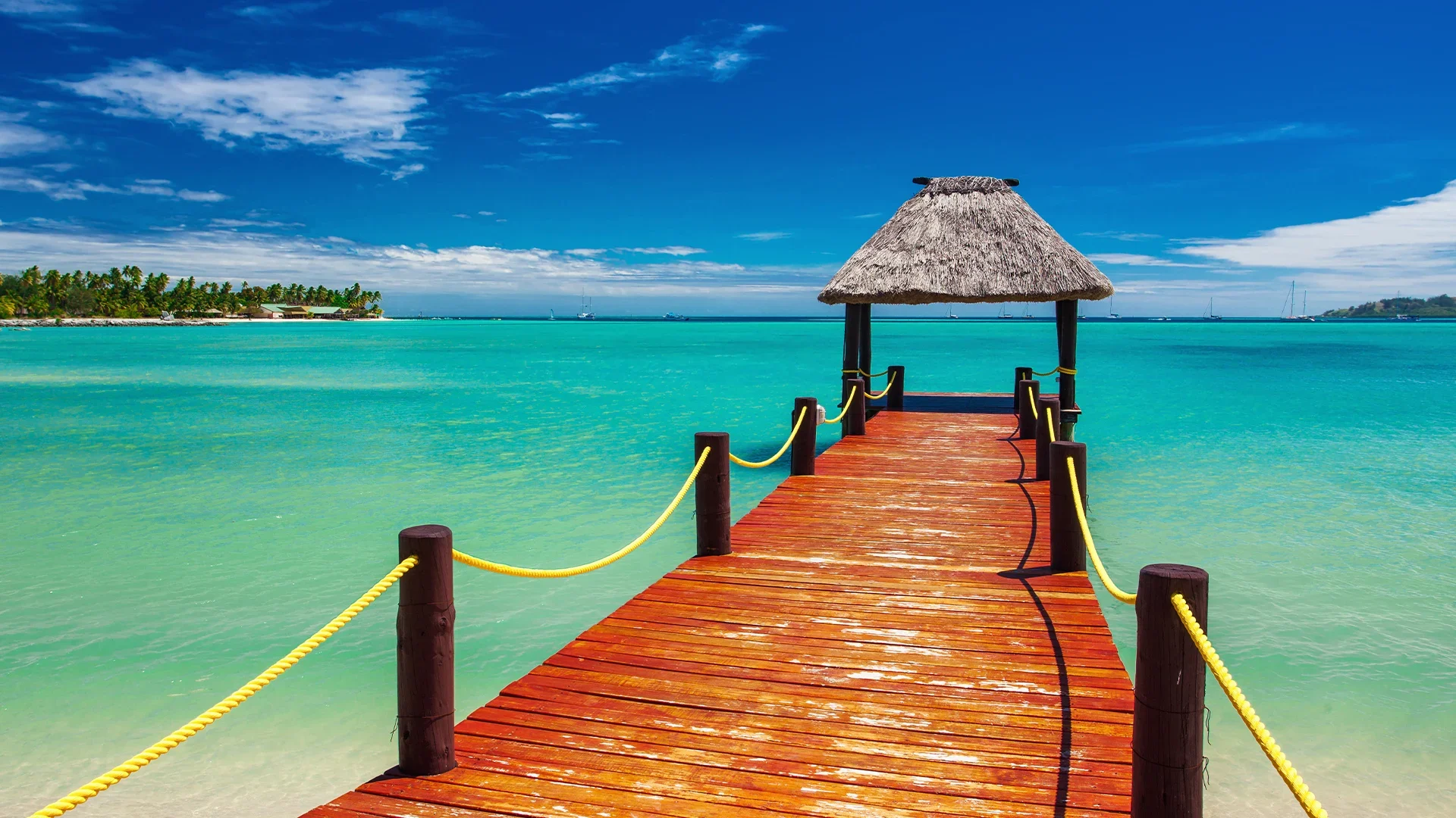 A wooden pier leading to a thatched hut on a tropical beach.