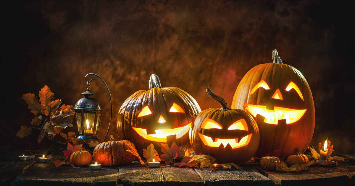 A group of lit jack-o-lanterns of different sizes, surrounded by autumn leaves and candles.