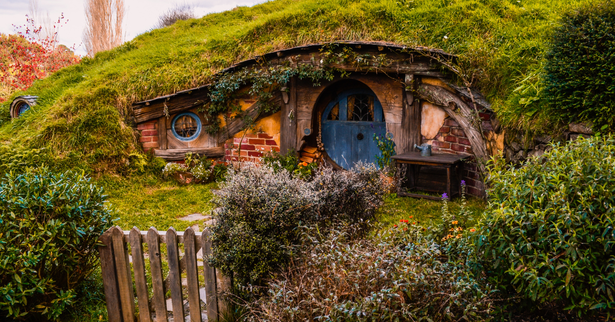 A hobbit hole with a round green door, surrounded by a lush garden and a picket fence.