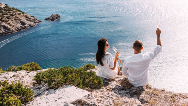A couple sitting on a cliff, drinking champagne while enjoying an ocean view.