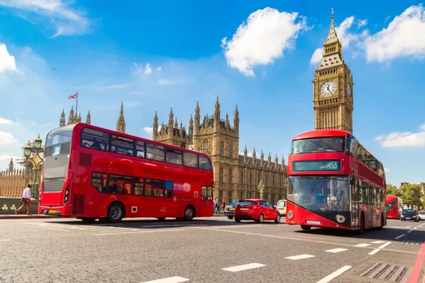 A view of Big Ben and the Houses of Parliament with red double-decker buses on the road in London.
