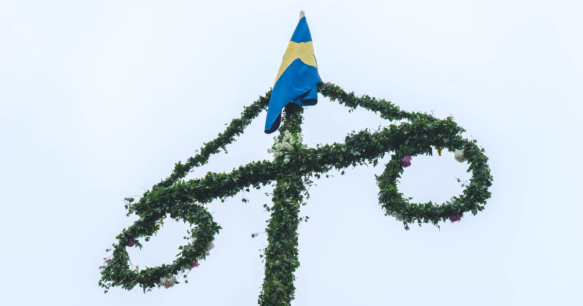 A close-up of a beautifully decorated Swedish Maypole, adorned with colorful flowers, greenery, and the Swedish flag.