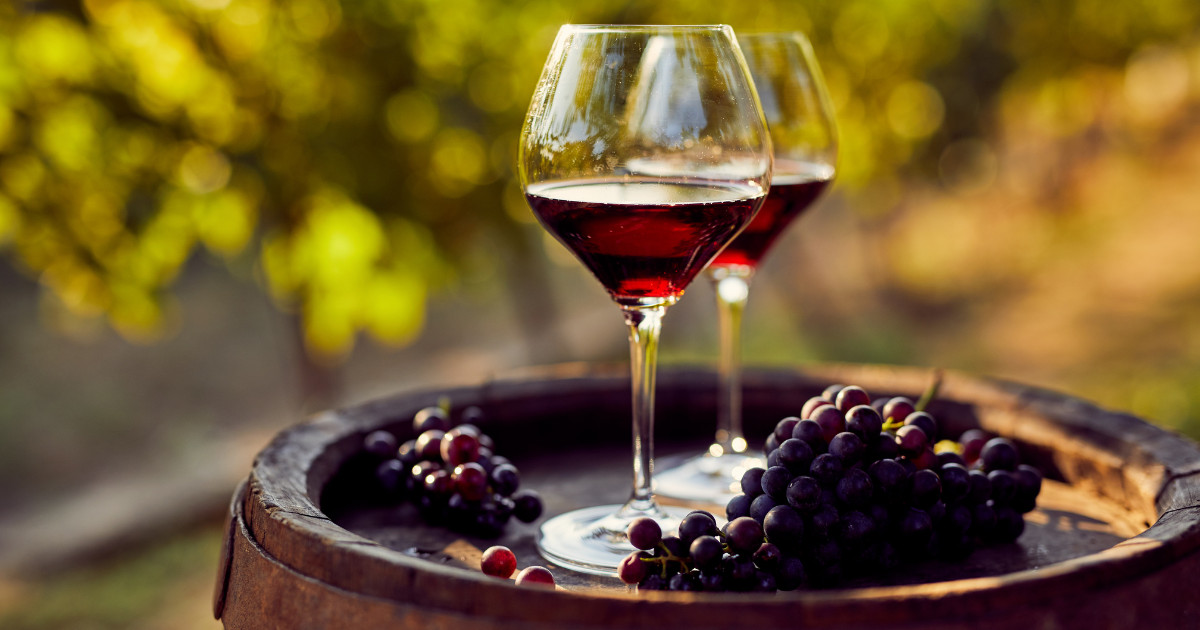 Two glasses of red wine with grapes on a barrel.