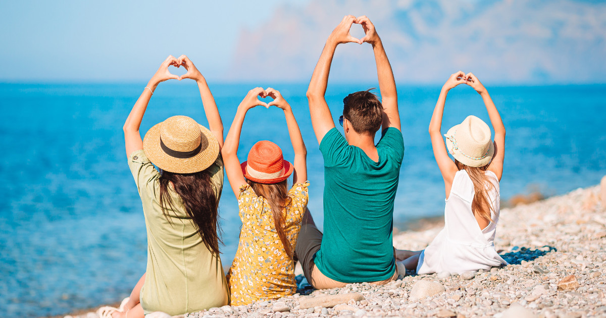 A family of four on the beach creating a heart shape with their hands