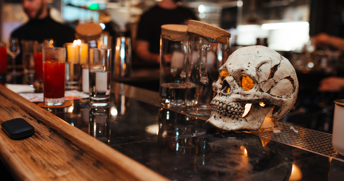 A white skull with glowing eyes, sitting on a bar counter with drinks and bar tools, creating a spooky atmosphere.