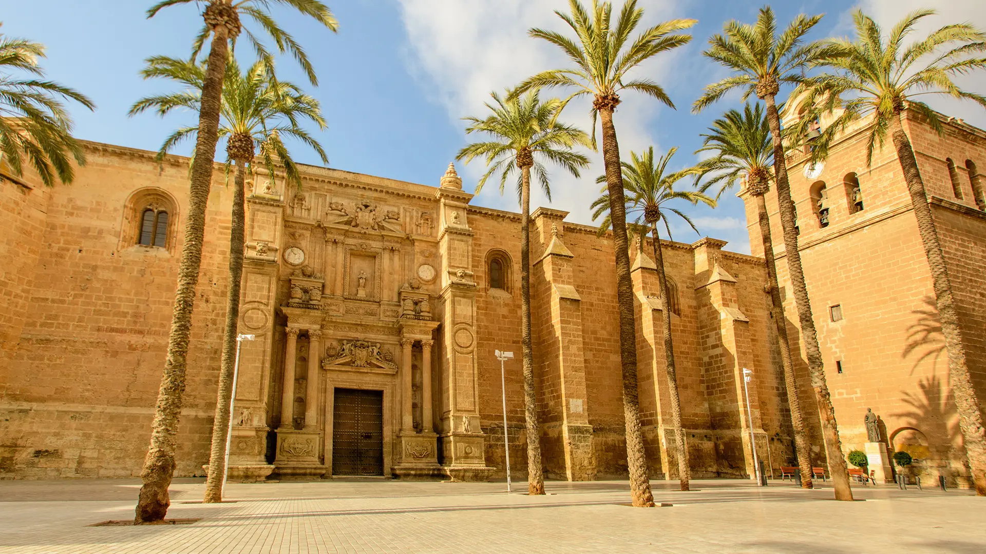 The historic Cathedral of Almería, a Renaissance-style cathedral with a beautiful facade, surrounded by tall palm trees.