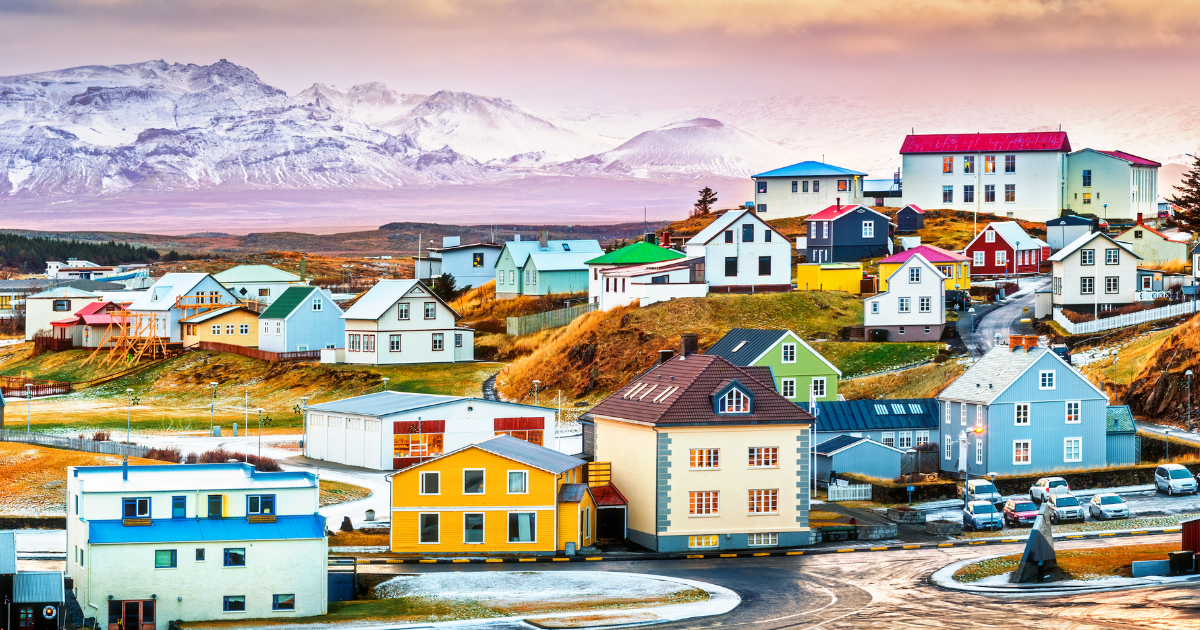 A vibrant town with colorful houses nestled against a backdrop of snow-capped mountains in Iceland, with a beautiful sunset sky.