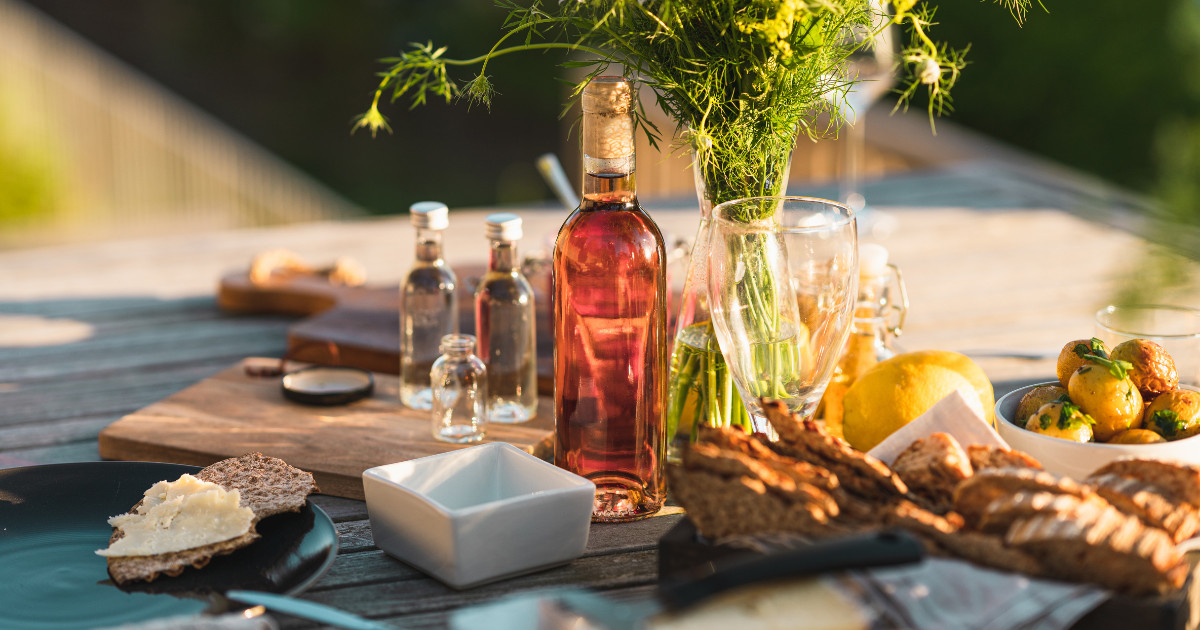 A beautifully set table with a bottle of wine, cheese, bread, and a vase of flowers, perfect for a summer evening meal.