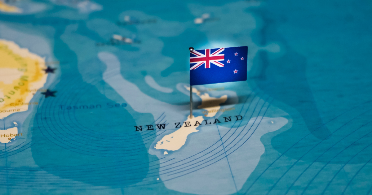 A close-up of the New Zealand flag pinned to a map of the world, highlighting the country's location.