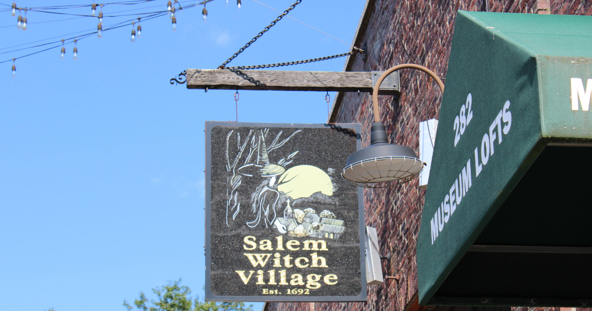 A vintage sign for the Salem Witch Village, featuring a witch and moon against a blue sky.