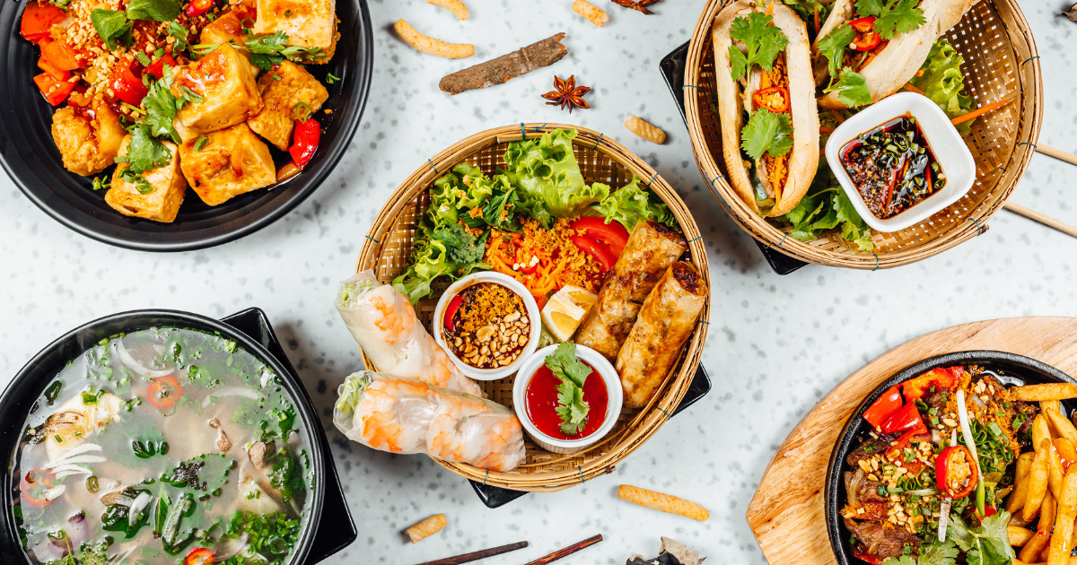 A selection of Vietnamese dishes, including spring rolls, Pho, and stir-fried tofu, arranged on a table with chopsticks and sauces.