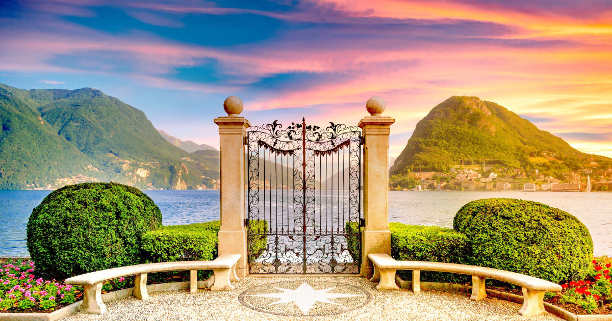 Lake Como in Italy, framed by a wrought iron gate, with mountains in the background and a colorful sunset sky.