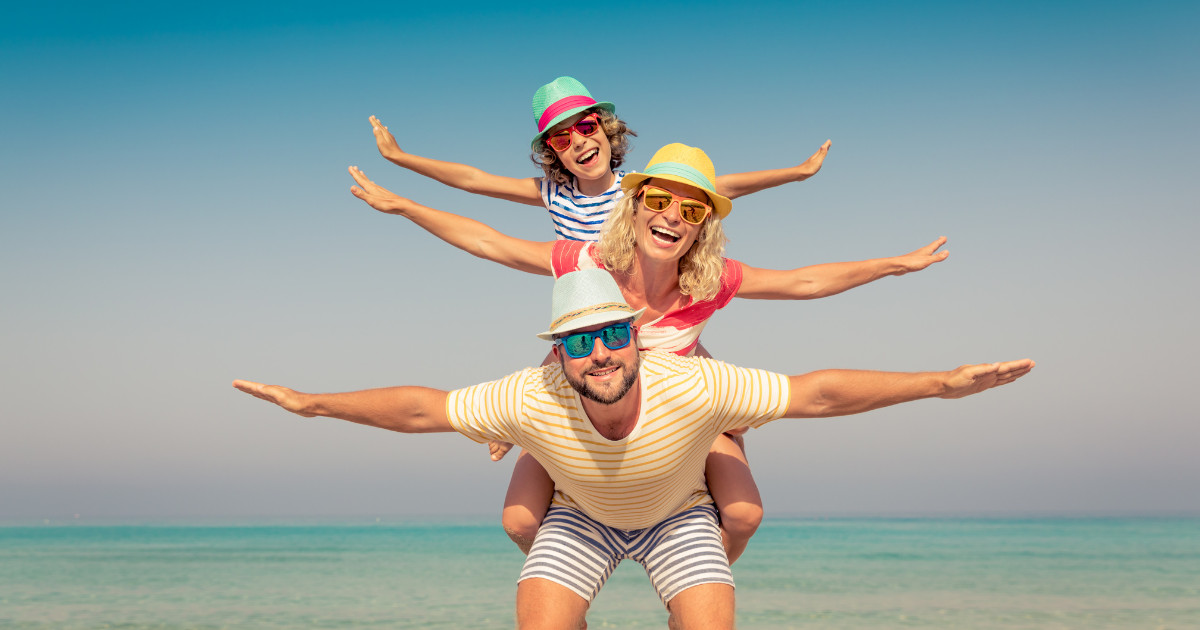 Happy family at the beach stacked in a playful pose with arms outstretched like airplane wings.