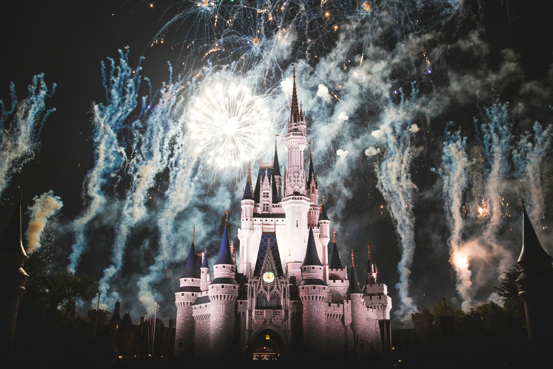 The iconic Cinderella's Castle at Walt Disney World, illuminated with fireworks bursting in the night sky.