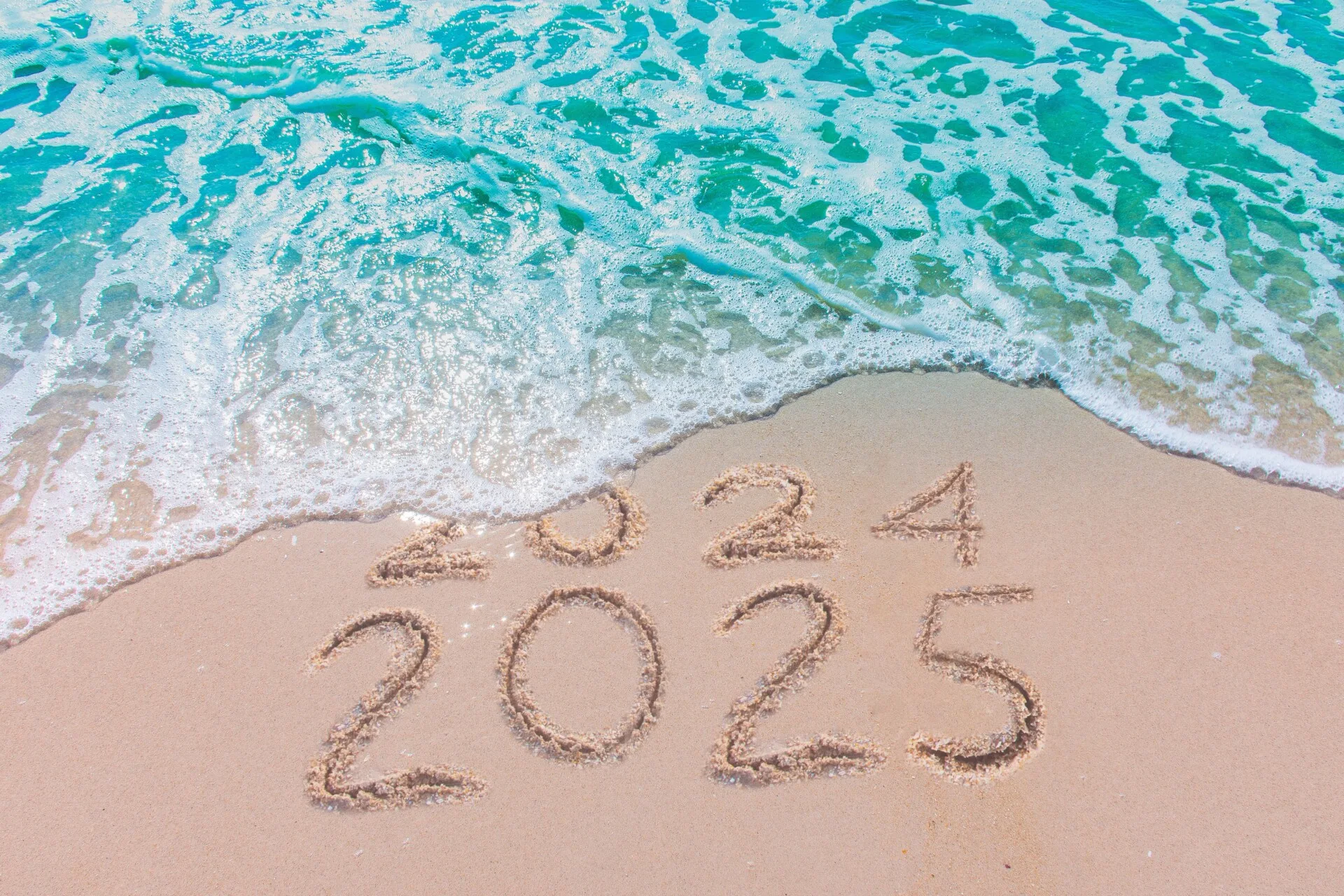 Beach. Water washing 2024 away with 2025 written in the sand.